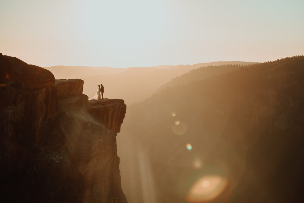 Bride and groom stand at the edge of Taft Point in Yosemite National Park, surrounded by golden sunset light and dramatic views of the valley and granite cliffs below. Captured during their adventurous elopement, this image highlights the storytelling style of The Pinckards, a destination elopement photo and video team focused on authentic, emotional moments in epic landscapes.