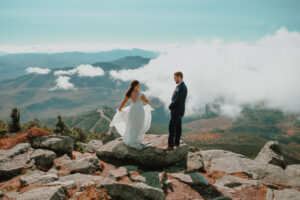 Bride dancing around in wedding dress on Whiteface Mountain in the Adirondacks while groom watches smiling
