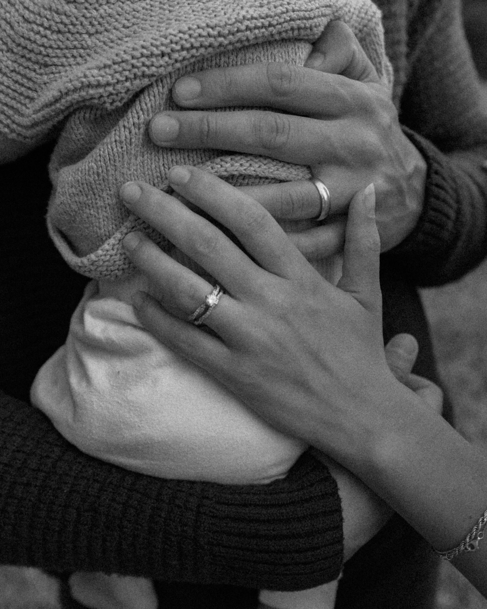 Closeup black and white photo of parents' hands on baby's back