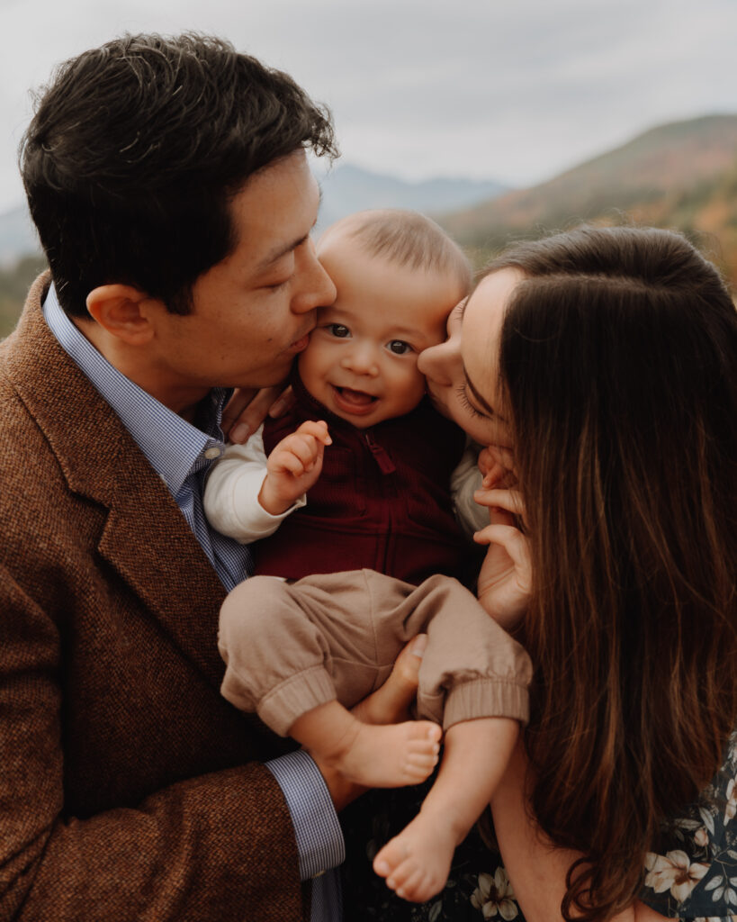 Parents kissing baby as he smiles right at the camera